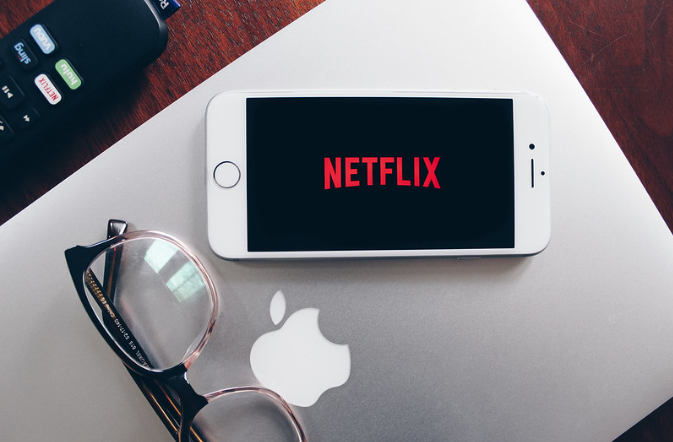 Netflix on a phone with a MacBook and glasses.