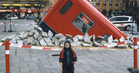This is an image of a little boy posing in front of a fake bus that crashed into the ground.